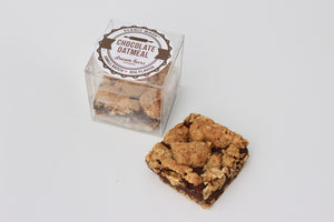 The chocolate oatmeal dream bar features on silky chocolate filling sandwiched between 2 layers of oatmeal cookie base. They are packed in a clear, square, food-safe container with an attractive label on top.